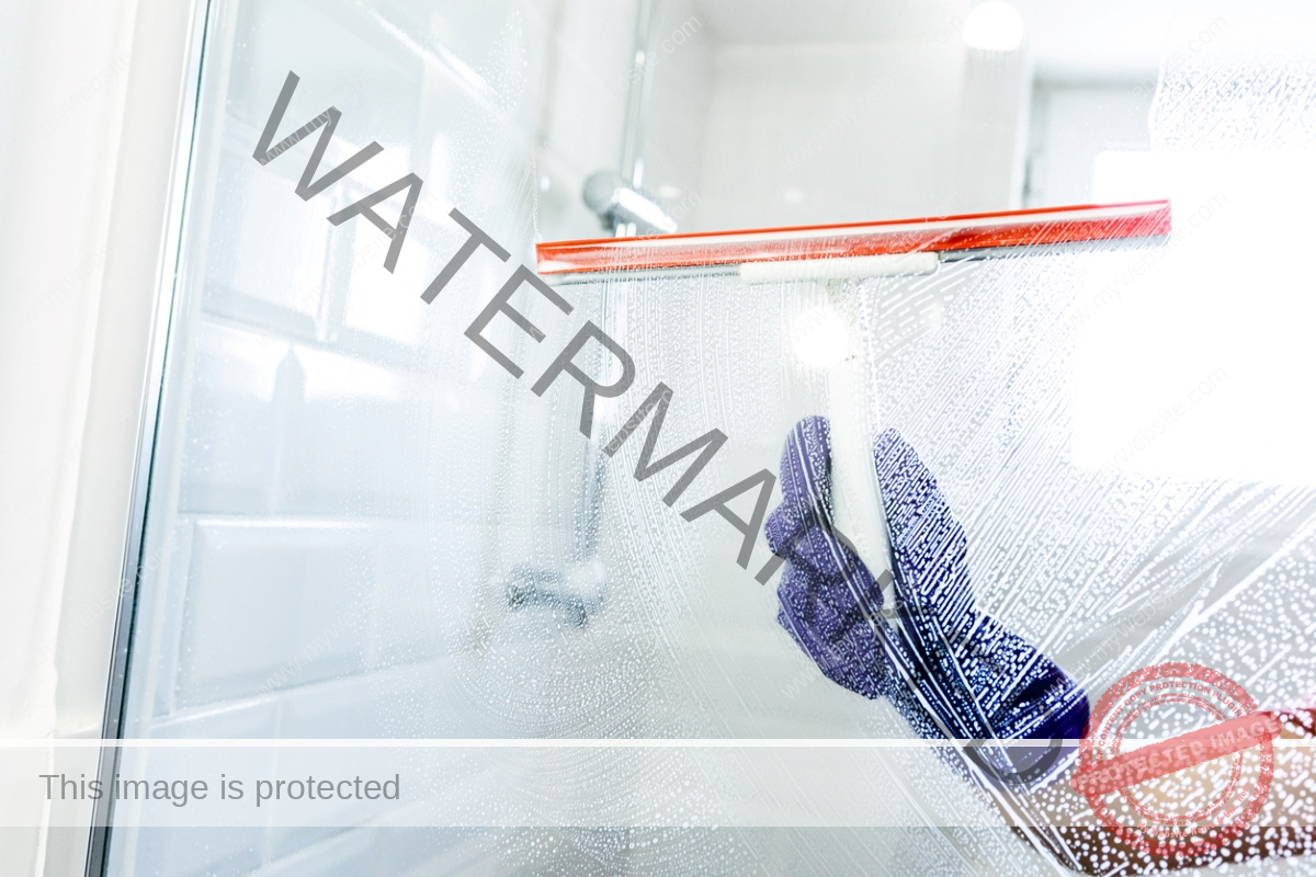 Man using squeegee on shower glass in bathroom.