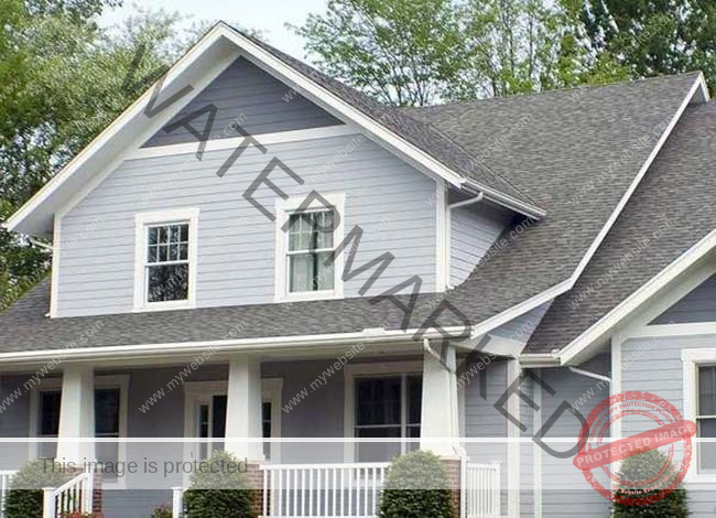 A light gray and blue house with a front porch, white decorations and bushes. 