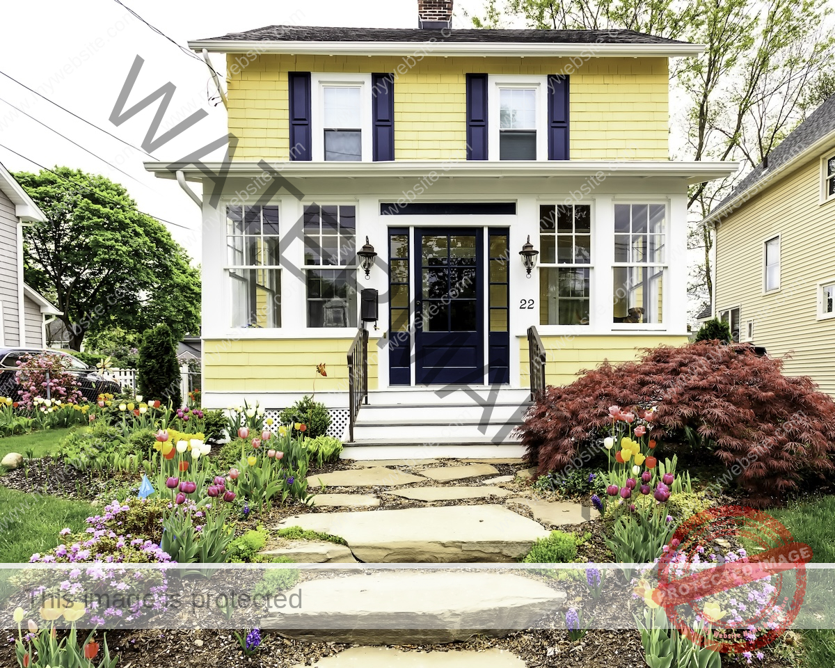 A yellow thatched house with a verandah and a stone path to the dark blue front door.