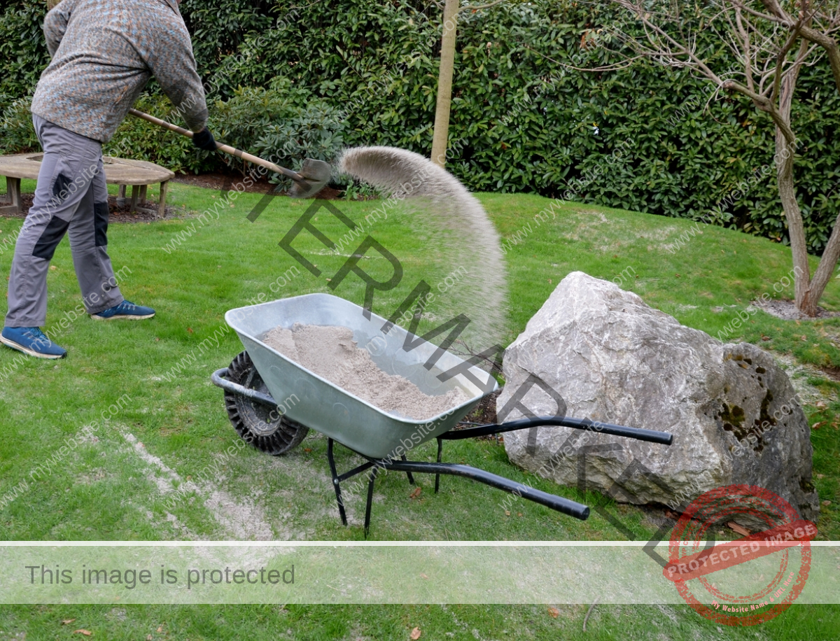 A person is taking out sand on the lawn with a cart.