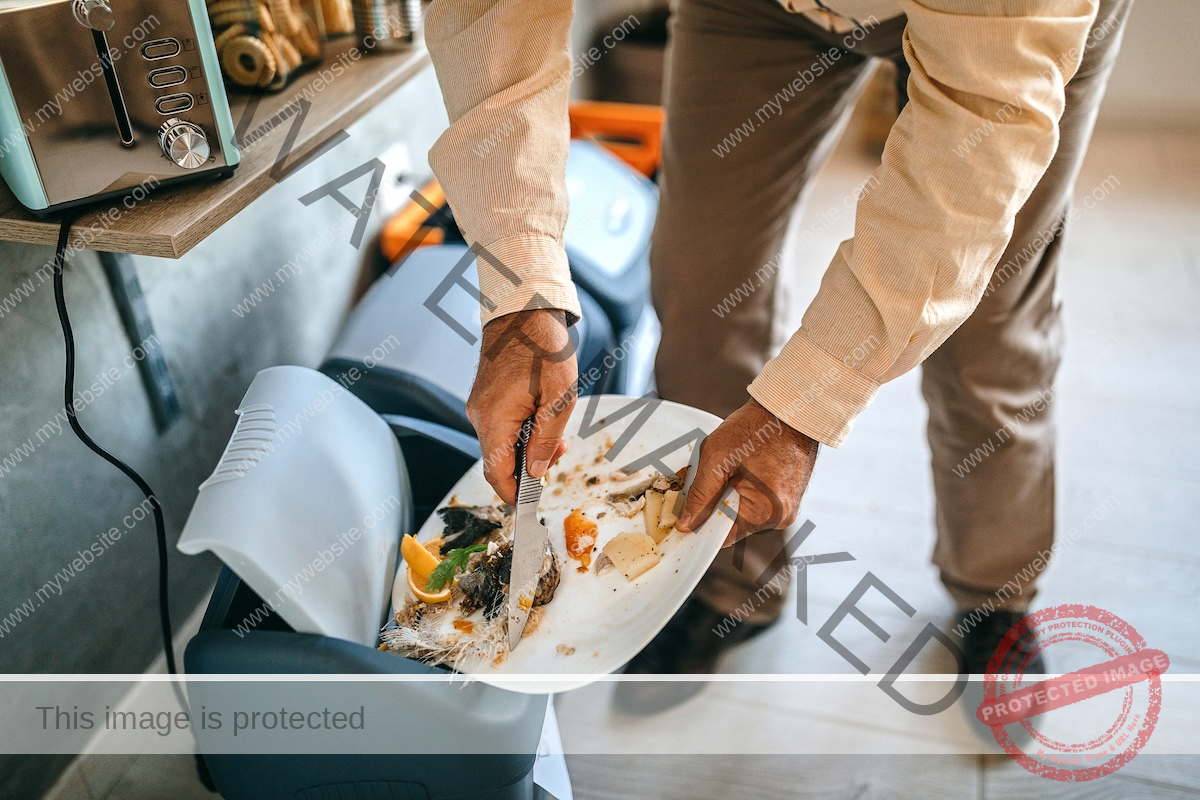 A man is throwing leftover food from his plate into the dustbin.