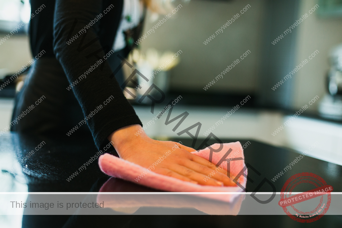 Close-up of a woman cleaning a black kitchen countertop with a pink cloth.