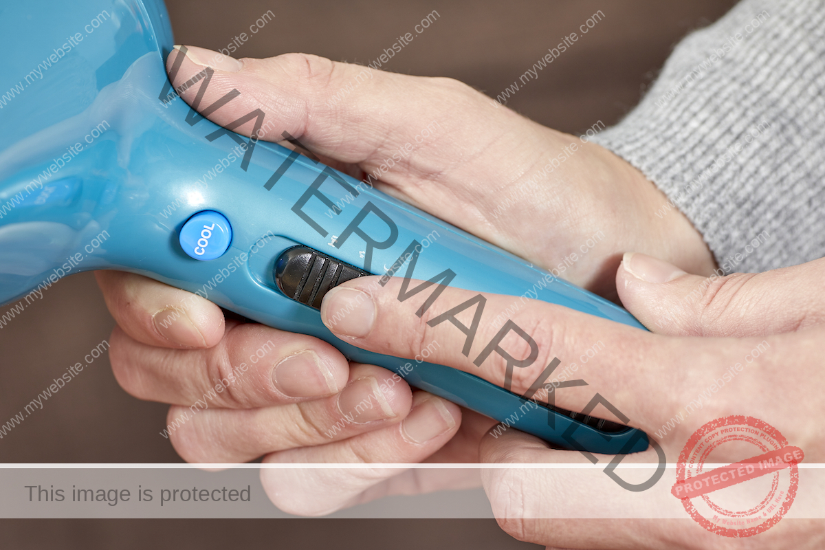 A woman sets her blue hair dryer on the lowest setting.