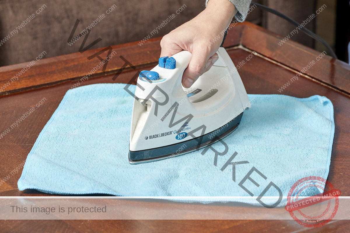 Woman ironing clothes on a microfiber cloth over a wooden table.