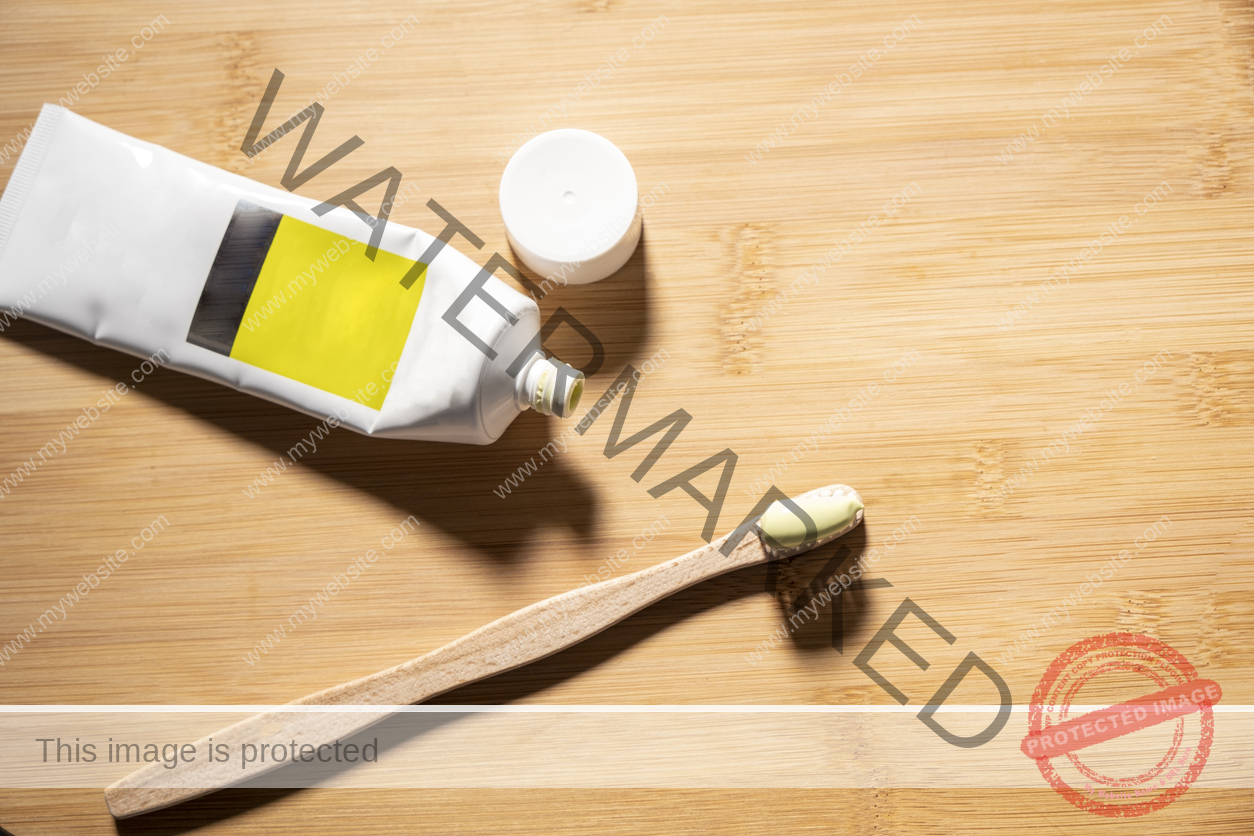 A toothbrush and an open tube of toothpaste on top of a wooden table.