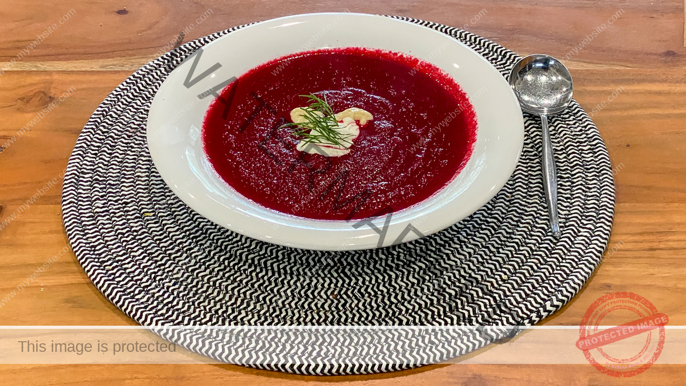 Bowl of borscht on top of a black and white placemat, which is on a wooden table.