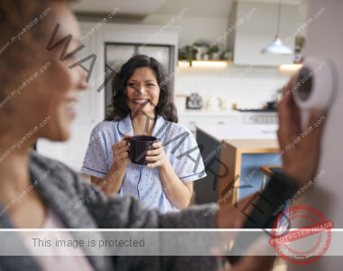 Woman adjusting smart thermostat, with another woman in the background.