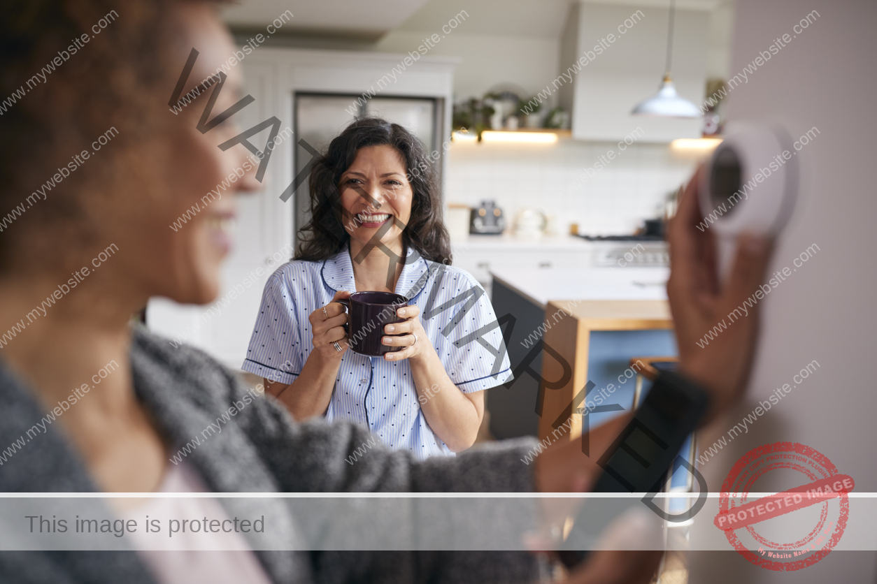 Woman adjusting smart thermostat, with another woman in the background.