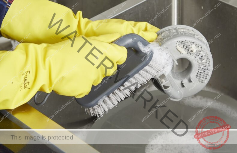 Clean the dishwasher filter with a hand scrub brush wearing yellow rubber gloves.