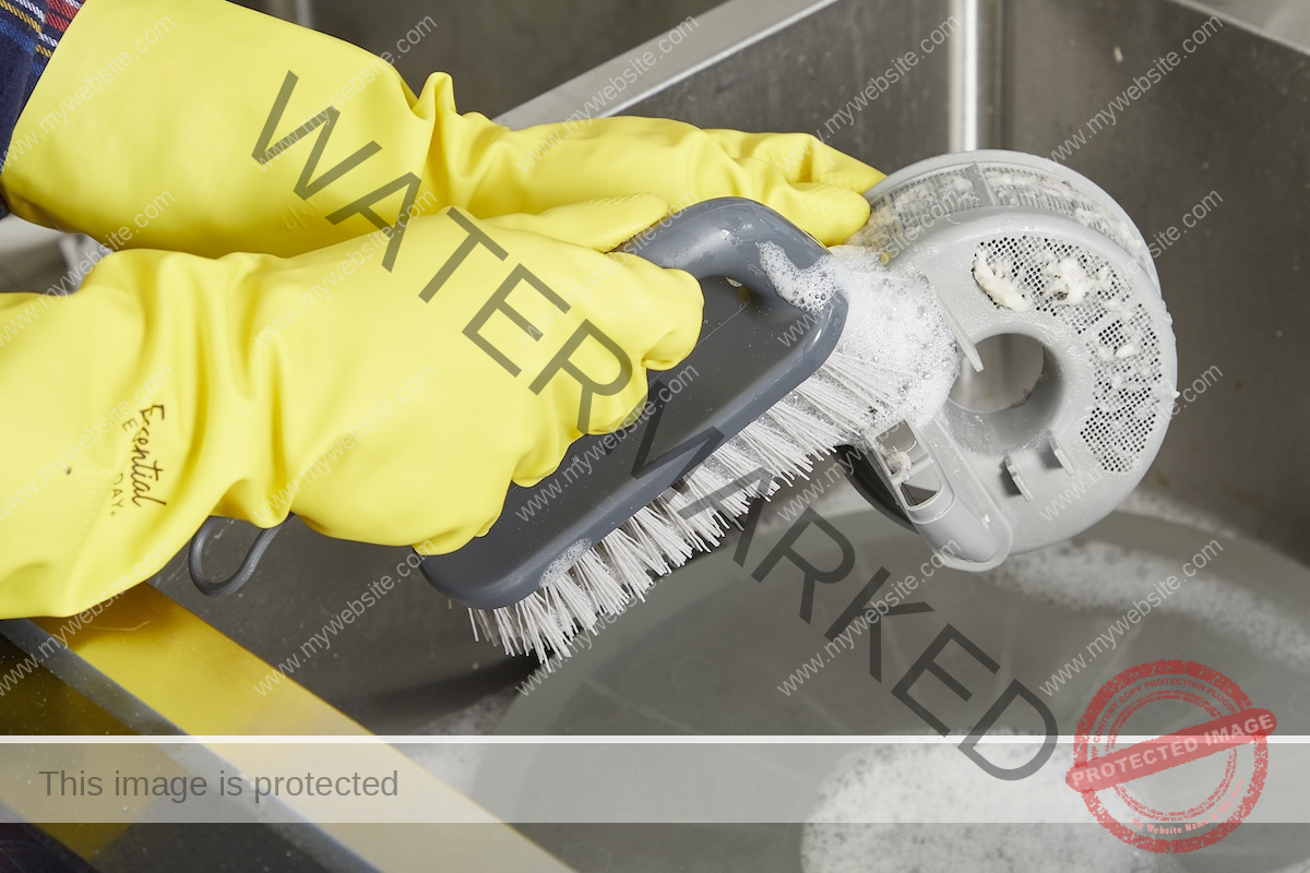 Clean the dishwasher filter with a hand scrub brush wearing yellow rubber gloves.