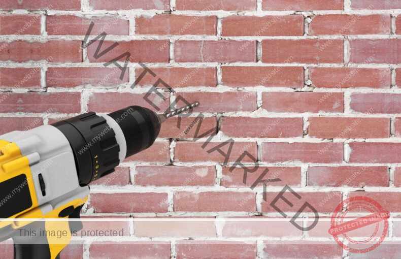 A yellow drill is being used to make a hole in a brick wall.