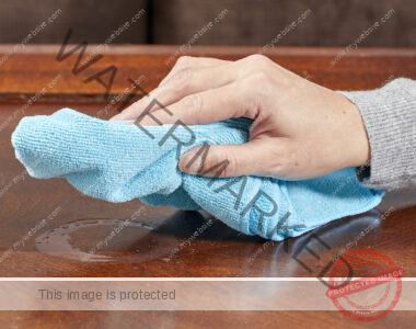 Woman uses microfiber cloth to wipe wet heat stain on table.