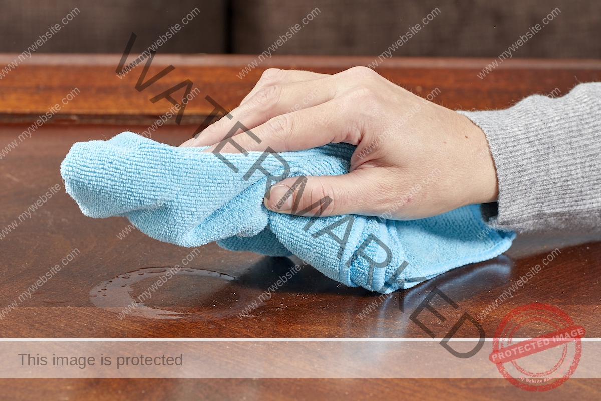 Woman uses microfiber cloth to wipe wet heat stain on table.